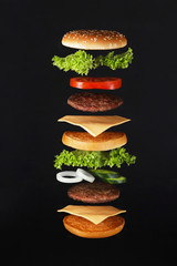 Flying burger ingredients. Delicious hamburger with flying ingredients on black background Flying...