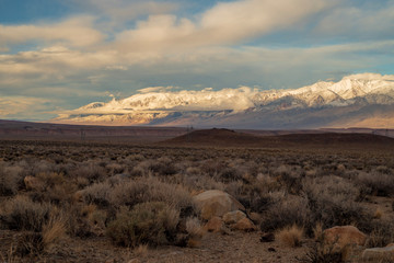 rocky desert, hills, distant clouds and snowy peaks of Sierra Nevada mountain range, California