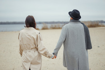 Young attractive girl and man walk along a deserted sandy beach. Romantic mood. Couple in love. Street shot.