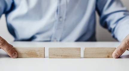 Businessman in a blue shirt arranges wooden jigsaw blocks. The man arranges empty blocks one on top of the other. Different concepts to supplement with content. Business concept, HR.