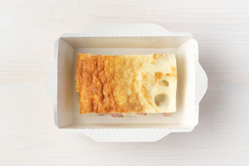 Omelet with sausage in paper luanch box on white wooden background