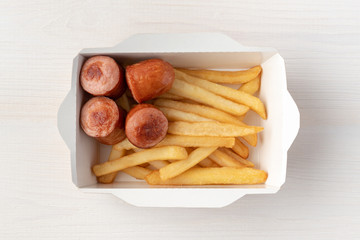 French fries and sausage in paper box on whitw wooden background