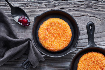 Camembert cheese baked in small iron cast skillets, top view on dark textured background