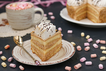 Honey sponge cake with butter cream located on a dark background. In the foreground a piece of cake on a plate