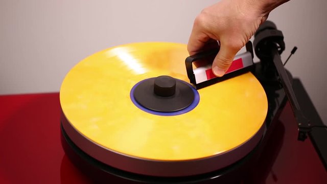 Close up view of a man cleaning yellow vinyl disc and putting down needle for playing record on audio record player.