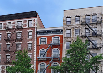old New York apartment building with external fire escapes, window air conditioners, and ornate trim around windows
