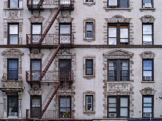 old New York apartment building with external fire escapes, window air conditioners, and ornate...