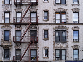 old New York apartment building with external fire escapes, window air conditioners, and ornate trim around windows