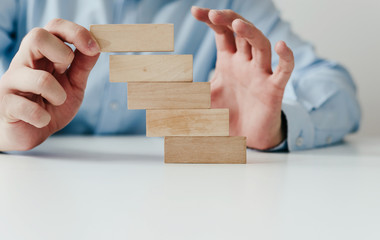 Businessman in a blue shirt arranges wooden jigsaw blocks. The man arranges empty blocks one on top of the other. Different concepts to supplement with content. Business concept, HR.