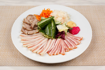 Meat and lard with vegetables on a white plate on the table.