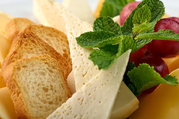 Exquisite festive snack closeup. Traditional Swiss, French, Italian, European delicacy for the holiday table, buffet, party. Bread, cheese, grapes and fresh mint on a plate.