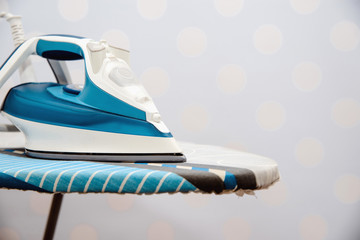 A blue modern iron on a blue, pastel background. The concept of ironing, taking care of your clothes. Ready to iron clothes after washing.
