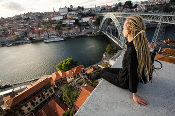 Woman with blond dreadlocks sitting in front of Douro river and Dom luis I bridge, Porto - Portugal.