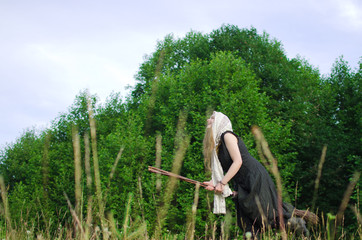 young witch is flying on a broomstick over a field among wild herbs