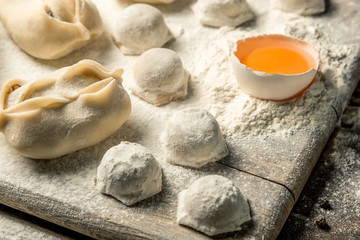Uzbek national food Chuchvara, like dumplings, on a wooden board, lie in flour with an egg