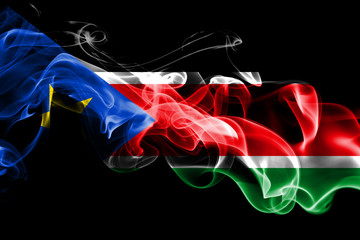 National flag of South Sudan made from colored smoke isolated on black background. Abstract silky wave background.