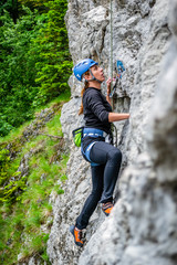 Beginner female climber on top rope, climbing a sport route near Sinaia town, in Bucegi mountains, Romania, on a chilly Spring day. Strong, active girl with helmet, harness and climbing shoes.