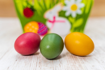 Obraz na płótnie Canvas Three colorful Easter eggs in front of felt Easter basket with wooden background