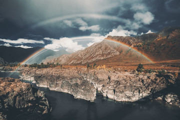 A stunning double rainbow over two banks of a mountain river Katun in Altai mountains, Russia: dark-blue stormy sky, rare clouds, autumn meadows overgrown with native grasses, cliffy riverside - obrazy, fototapety, plakaty