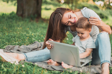 Mother with son sitting in the park and work on laptop.