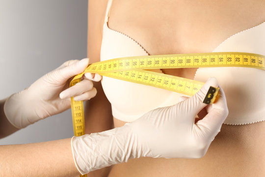 Doctor measuring size of patient's breast on gray background, closeup. Cosmetic surgery