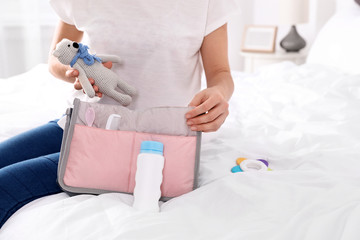 Obraz na płótnie Canvas Woman packing baby accessories into maternity bag on bed, closeup