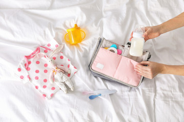 Woman packing baby accessories into maternity bag on bed, top view