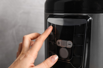 Woman turning on modern electric multi cooker on grey background, closeup