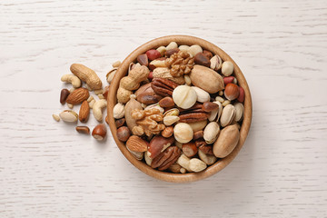 Bowl with organic mixed nuts on white wooden background, top view