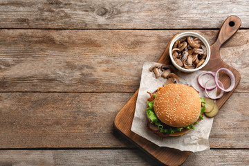 Tasty burger and mushrooms on wooden background, top view. Space for text