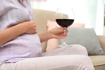 Future mother with glass of wine at home, closeup. Alcohol abuse during pregnancy
