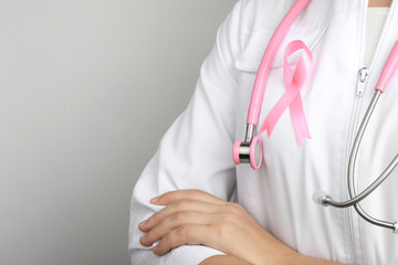 Doctor with pink ribbon and stethoscope on grey background, space for text. Breast cancer awareness