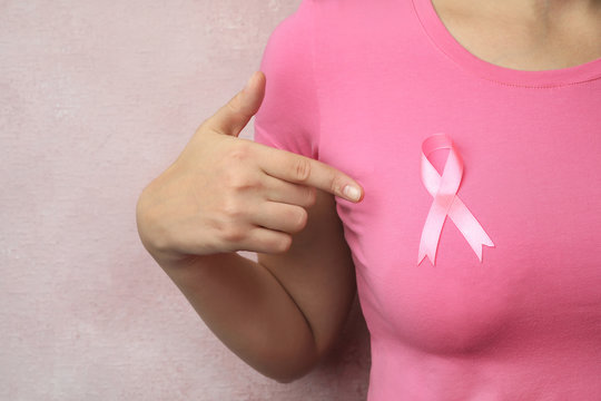 Woman with pink ribbon on color background, closeup. Breast cancer awareness