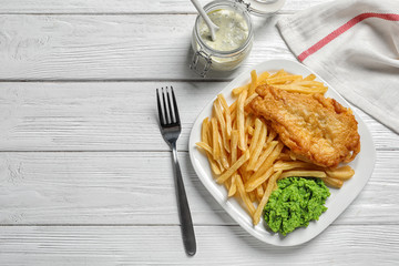Plate with British traditional fish and potato chips on wooden background, top view. Space for text