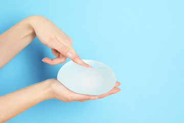 Woman touching silicone implant for breast augmentation on color background, space for text....