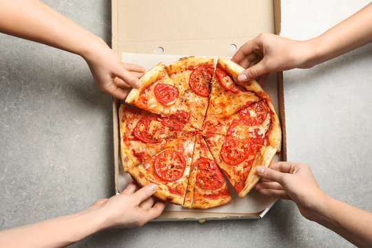 Young people taking slices of hot cheese pizza from cardboard box at table, top view. Food delivery service