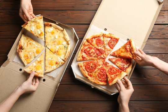 Young people taking slices of hot cheese pizzas from cardboard boxes at table, top view. Food delivery service