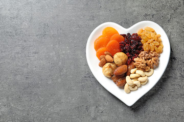 Heart shaped plate with different dried fruits and nuts on table, top view. Space for text