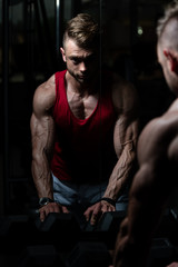 Fototapeta na wymiar Handsome Young Man Standing Strong In The Gym And Flexing Muscles - Muscular Athletic Bodybuilder Fitness Model Posing After Exercises