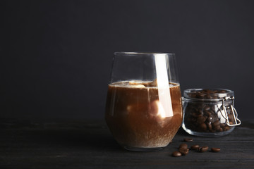 Coffee drink with milk ice cubes and beans on table against dark background. Space for text