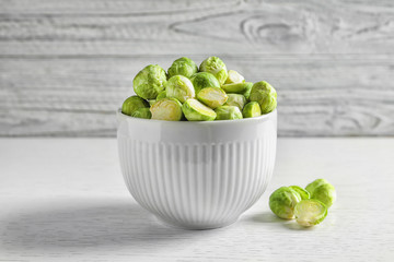 Bowl of fresh Brussels sprouts on table against wooden background