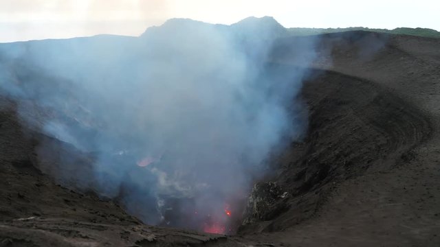 Mount Yasur exploding and belching out mist and hot pieces of glowing magma. Dark clouds of smoke rise from the base of the deep crater on a remote tropical island in Pacific. Stunning active volcano.