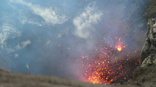 CLOSE UP: Scorching hot lava flies out of the active crater of Mount Yasur. Active volcano in Sicily violently blasting the glowing orange pieces of lava high in the air. Smoke rising from the crater.