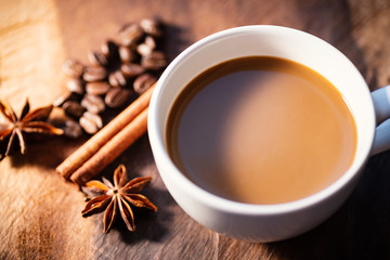 Cup of coffee with cinnamon stick, star anise and roasted coffee beans on wooden table, hot drink