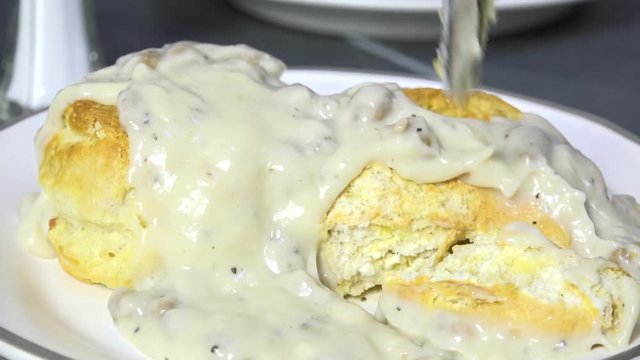 Spooning country gravy with sausage on biscuits slow motion
