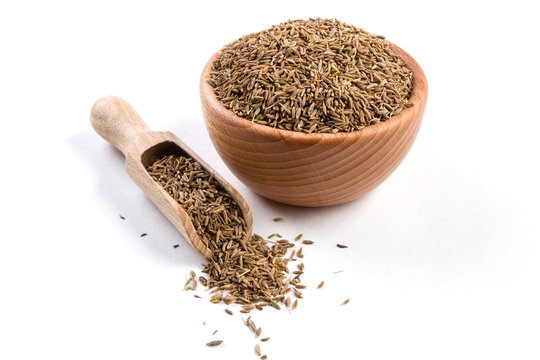 Cumin in wooden bowl and scoop isolated on white background. Closeup.