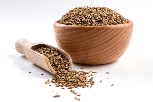 Cumin in wooden bowl and scoop isolated on white background. Closeup.