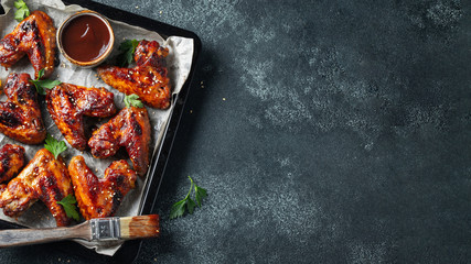 Roasted chicken wings in barbecue sauce with sesame seeds and parsley in a baking tray on a dark...
