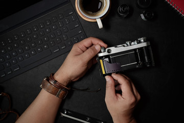 Man hand loading film 35mm on vintage camera at dark leather desk