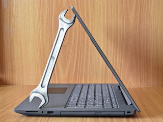 Concept of computer repair and maintenance. Metal wrench holds notebook open cover of lcd display on wooden table. Side view